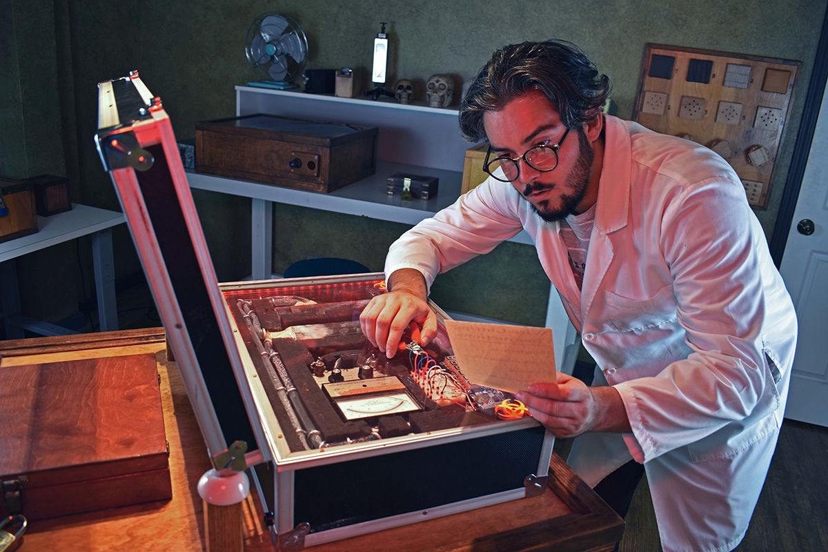Scientist in a lab coat solving an electronics puzzle case in The Mad Scientist escape room at Brain Games.